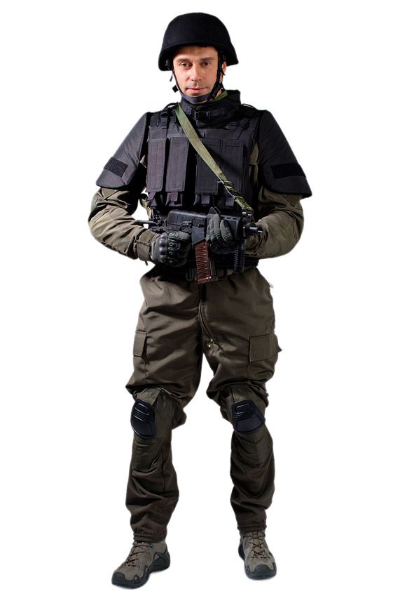 Военный в черном шлеме и синем бронежилете стоит с оружием в руках ракурс анфас