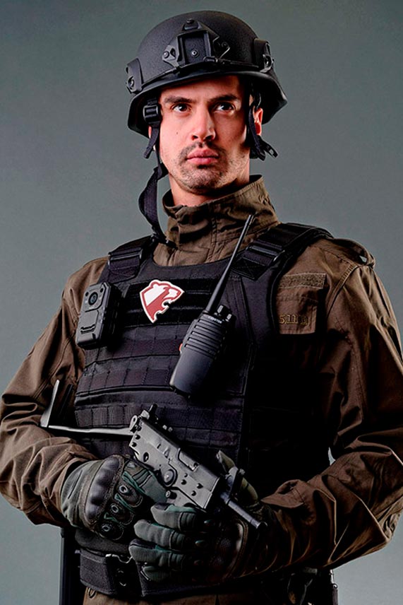 Мужчина в черном бронежилете и шлеме с пистолетом-пулеметов в руках смотрит в даль